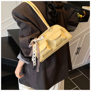 Macro detail of yellow patent leather shoulder bag featuring dual pockets and plaid ribbon bow