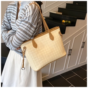 Detail of cream woven tote bag featuring brown leather straps and metal hardware accents