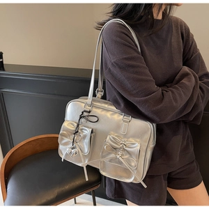 Dettaglio della borsa tote argento metallizzato con fiocchi e ciondolo a cuore in metallo