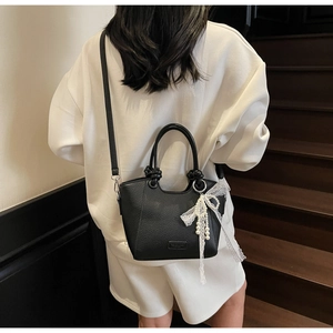 Détail du sac cabas en cuir grainé noir avec charme en perles et nœud en dentelle