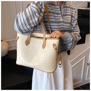 Detail of a large woven cream tote bag with brown leather handles and side D-ring
