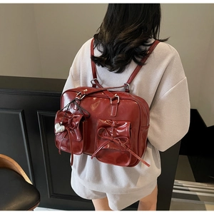 Dettaglio di uno zaino stile balletto rosso scuro lucido con fiocchi e ciondolo a cuore