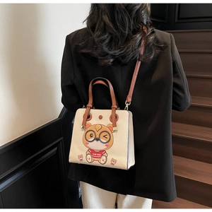 Detailed view of cream tote bag with cartoon design and brown leather straps worn by model