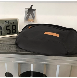 Détail d'un grand sac bandoulière noir avec logo en cuir marron sur une surface en métal