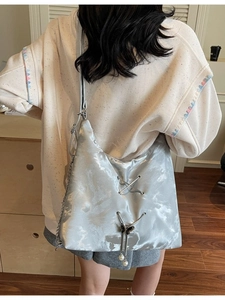 Silver satin tote bag with drawstring detail and butterfly charm shown in a crossbody style