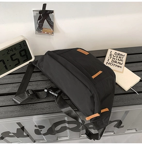 Détail du sac bandoulière en nylon noir avec tirette en cuir marron et boucle industrielle