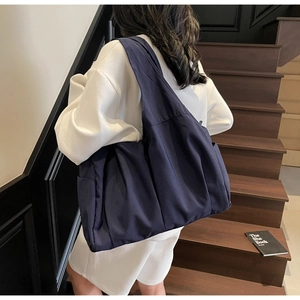 Détail d'un grand cabas en nylon bleu marine avec design plissé porté par un mannequin