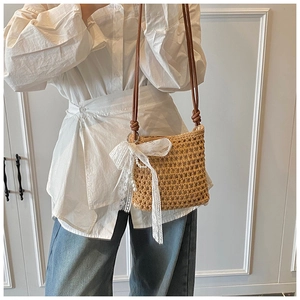 Détail du sac en paille avec un grand nœud en dentelle blanche et pendentif perle