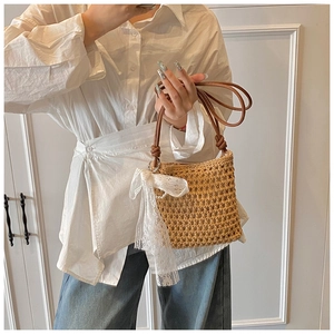 Détail du sac en paille tissée avec nœud en dentelle blanche et bandoulière en cuir marron