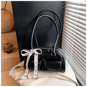 Detail of black glossy handbag with front flap pockets and a checkered ribbon bow