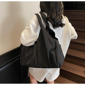 Détail d'un sac cabas en nylon noir avec texture plissée porté à l'épaule par un mannequin