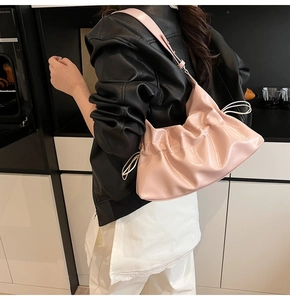 Détail du sac seau nuage rose plissé porté par un mannequin dans un décor urbain élégant