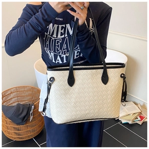 Detail showing high-capacity cream woven tote bag with contrast black handles and metal ring