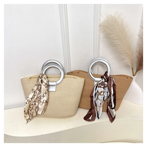 Detail of woven straw tote bags in beige and brown with metal handles and silk scarves