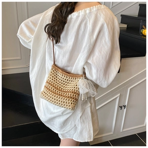 Détail d'un sac bandoulière en paille tressée avec nœud en dentelle et pompon perlé