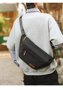 Détail du sac bandoulière noir montrant la tirette en cuir et l'écusson du logo de la marque