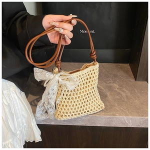 Détail d'un sac à main tressé beige avec bandoulière en cuir brun et nœud en dentelle