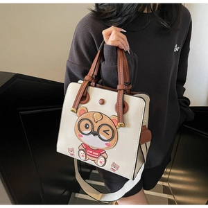 Close-up of off-white tote bag featuring a cute cartoon bear and wide striped shoulder strap