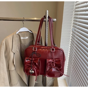 Dettaglio di una borsa tote in pelle lucida rosso scuro con eleganti fiocchi e ciondoli