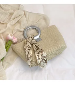 Detail of woven straw tote bag featuring silver circular handles and floral silk scarf accessory