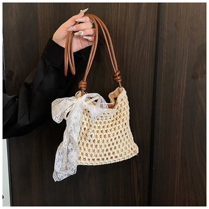 Détail d'un sac en paille avec des poignées en cuir marron et un nœud en dentelle blanche