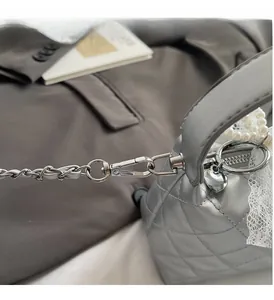 Detail of silver quilted handbag with metallic chain strap and luxury heart pendant