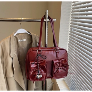 Dettaglio della borsa tote in pelle lucida bordeaux con fiocchi e ciondolo a cuore