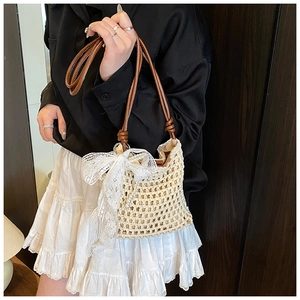 Détail du sac seau tissé avec un nœud en dentelle blanche et charms en perles