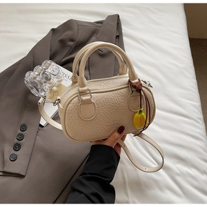 Close-up of cream bowling bag with textured leather, dual handles and banana charm