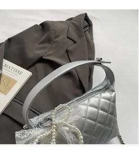 Detail of silver quilted pillow bag with pearl lace bow charm and metallic chain strap