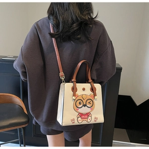 Close-up of off-white tote bag with cartoon print, brown handles and shoulder strap