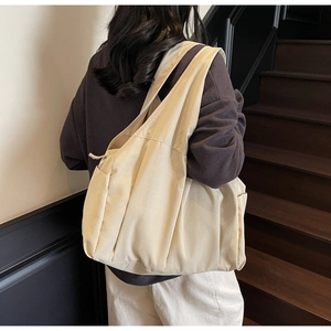 Détail d'un sac cabas en toile beige avec poche latérale sur un escalier en bois