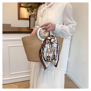 Detail of hand-woven straw tote bag with silver metal round handles and floral scarf