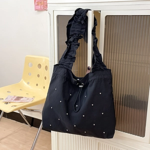 Detail of black nylon tote bag featuring ruffled shoulder straps and silver stud accents