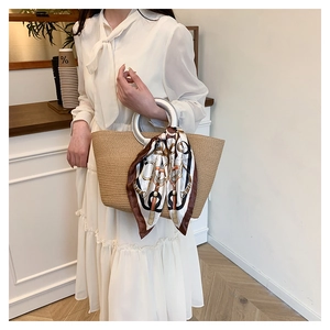 Detail of woven straw tote bag featuring silver round metal handle and decorative silk scarf