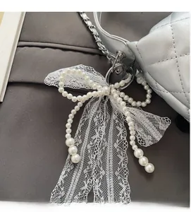 Detail of white pearl bow charm with lace ribbon on silver quilted chain bag