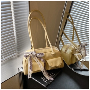 Detail of a creamy yellow Boston bag featuring twin front pockets and a plaid bow tie