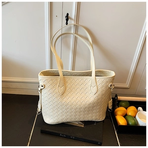 Close-up of creamy white woven tote bag with leather straps on a minimalist background