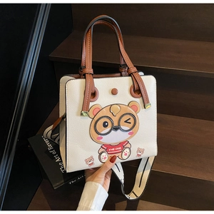 Close-up of white pebble leather tote featuring cartoon bear and striped strap
