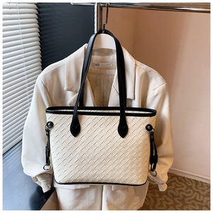 Close-up of cream woven tote bag featuring black leather trim and contrast details