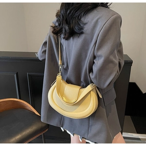Detailed view of yellow lychee leather saddle bag shown on a model in a grey suit