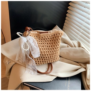 Détail du sac bandoulière en paille tressée avec nœud en dentelle et breloque en perles