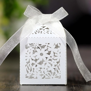 Close-up of white laser-cut hollow candy box with elegant floral pattern and organza ribbon bow