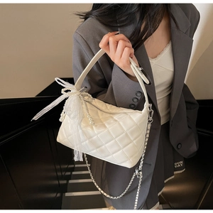 Detail of white quilted handbag with pearl lace bow charm and metal chain strap