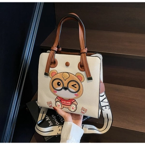 Close-up of beige tote bag with cartoon bear and wide LOVE strap on wooden stairs