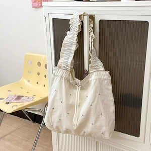 Detail of cream nylon tote bag featuring rhinestone accents and ruffled shoulder strap