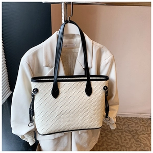 Detail of cream woven tote bag with black handles hanging on a metal hanger