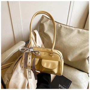 Detailed close-up of yellow glossy underarm bag with decorative ribbon and side pockets