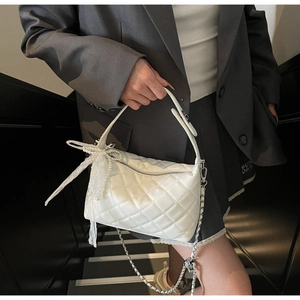 Detail of white quilted crossbody bag with lace bow and elegant pearl charm detail