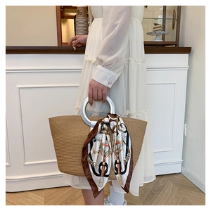 Detail of khaki woven straw tote bag with silver circular handle and patterned silk scarf